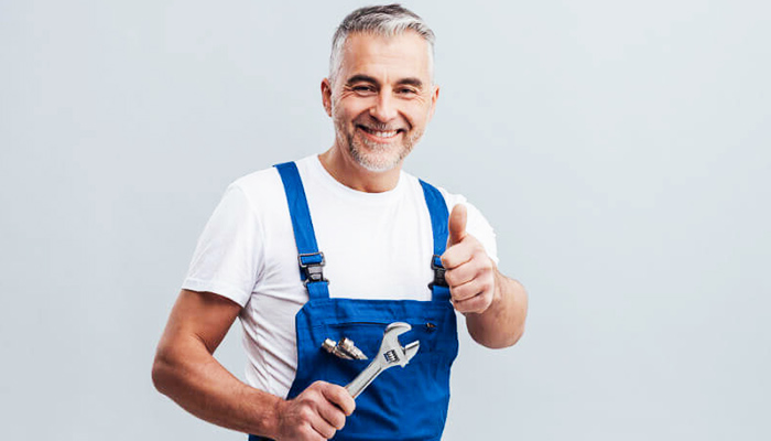 An older man wearing a white t-shirt and overalls holding a wrench