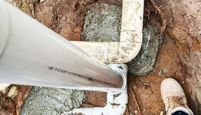 Two white pipes surrounded with dirt and cement 